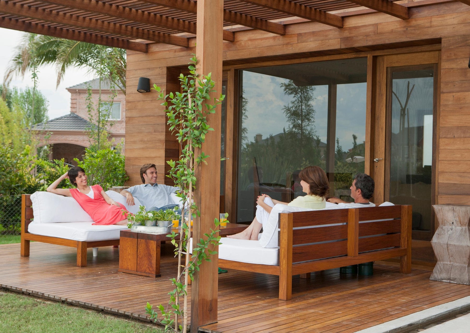 Group of friends relaxing and chatting on a wooden patio at an Airbnb, surrounded by greenery and modern outdoor furniture.