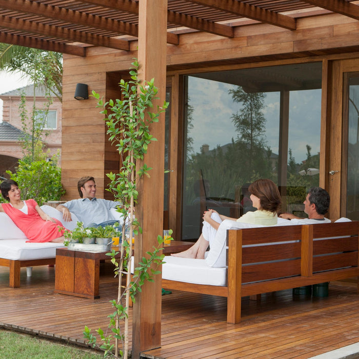 Group of friends relaxing and chatting on a wooden patio at an Airbnb, surrounded by greenery and modern outdoor furniture.