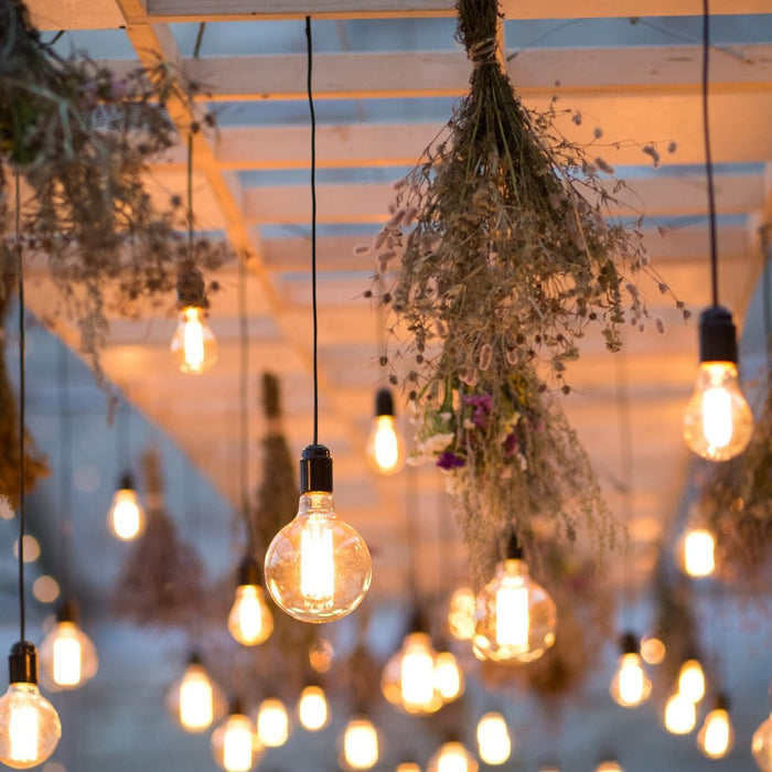 Hanging Edison-style string lights with dried floral décor under a pergola, creating a warm and inviting outdoor ambiance