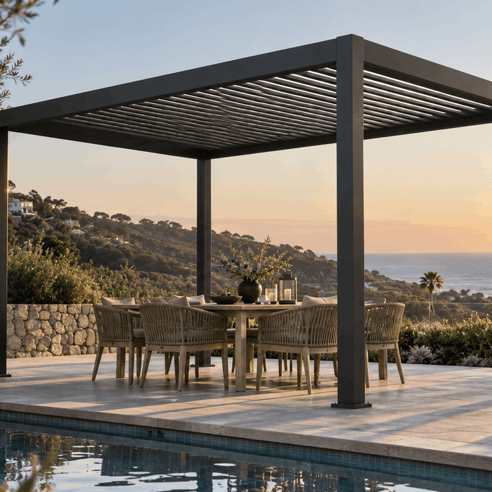 Black aluminum louvered pergola over a dining table beside a pool overlooking the ocean at sunset