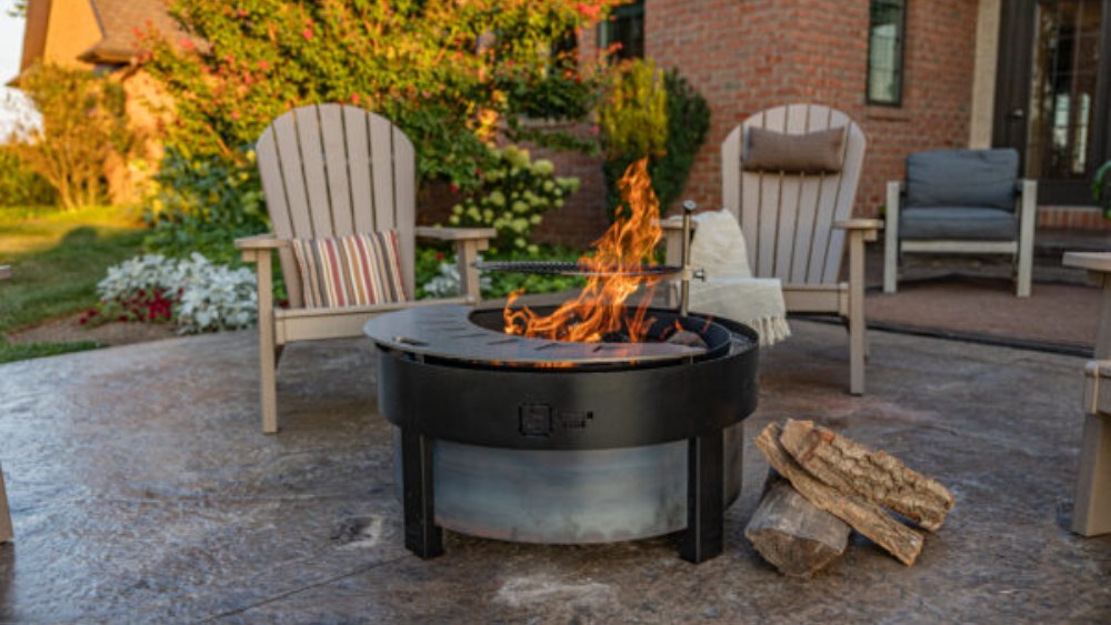 Yard Craft The Forge smokeless fire pit burning on a stamped concrete patio with Adirondack chairs at golden hour