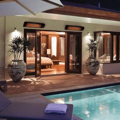 Three wall-mounted electric infrared patio heaters glowing over a covered poolside patio at a home in the evening