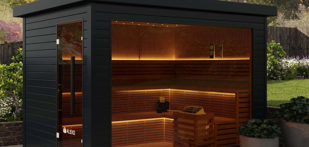 Black Aleko Camellia outdoor sauna with glass wall and lit cedar benches on a patio