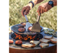Arteflame Classic 30" Grill with person cooking burgers and bread on flat-top corten steel surface over open flame
