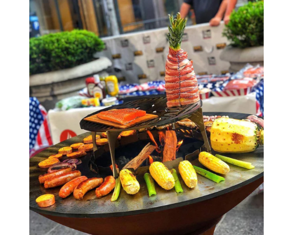 Arteflame Classic 40" Grill with Tall Euro Base grilling sausages, corn, salmon, and bacon-wrapped pineapple on flat-top