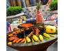 Arteflame Classic 40" Grill with Tall Euro Base grilling sausages, corn, salmon, and bacon-wrapped pineapple on flat-top