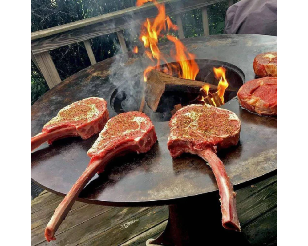 Arteflame Classic 40" Grill flat-top steel surface searing seasoned tomahawk ribeye steaks over open wood fire