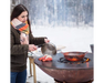 Arteflame Classic 40" Grill with woman cooking lobster tails on flat-top steel surface outdoors in winter snow setting