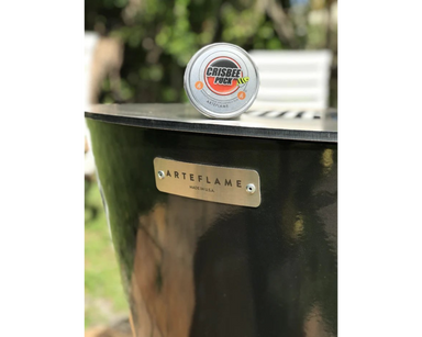 Crisbee Puck grill seasoning tin placed on Arteflame Made in USA black steel fire pit grill flat-top surface