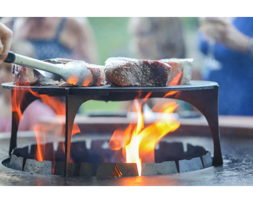 Arteflame Stainless Steel Grill Grate Riser elevating steaks over open flame in Arteflame fire pit grill center bowl