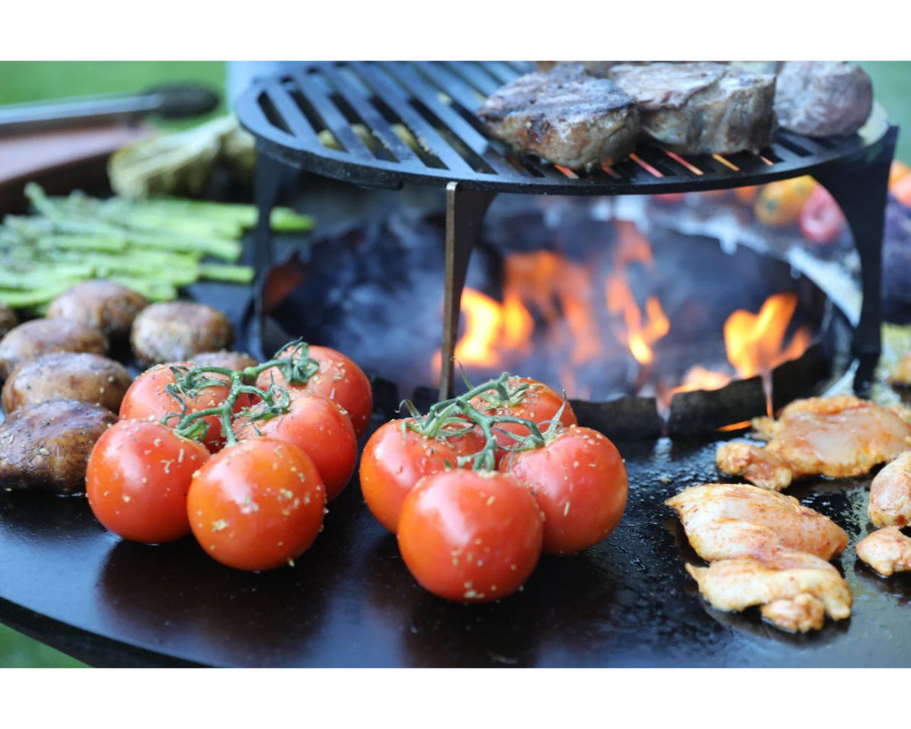 Arteflame Grill Grate Riser with steaks over open flame surrounded by tomatoes, mushrooms, asparagus, and chicken