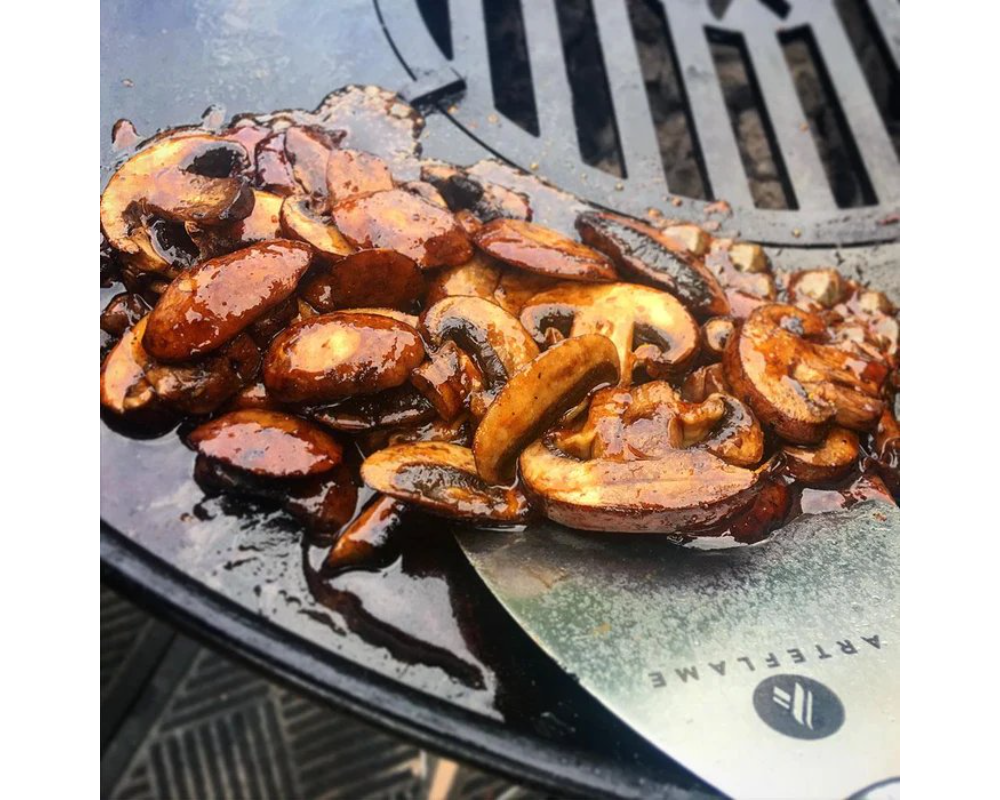 Arteflame Griddle Scraper cleaning sautéed mushrooms off Arteflame carbon steel flat-top grill cooktop surface
