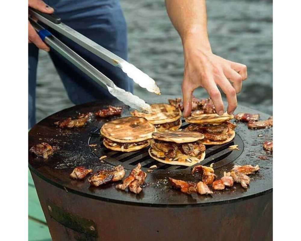 Arteflame One Series 20" Grill flat-top steel surface cooking meat-filled tacos and chorizo with stainless steel tongs