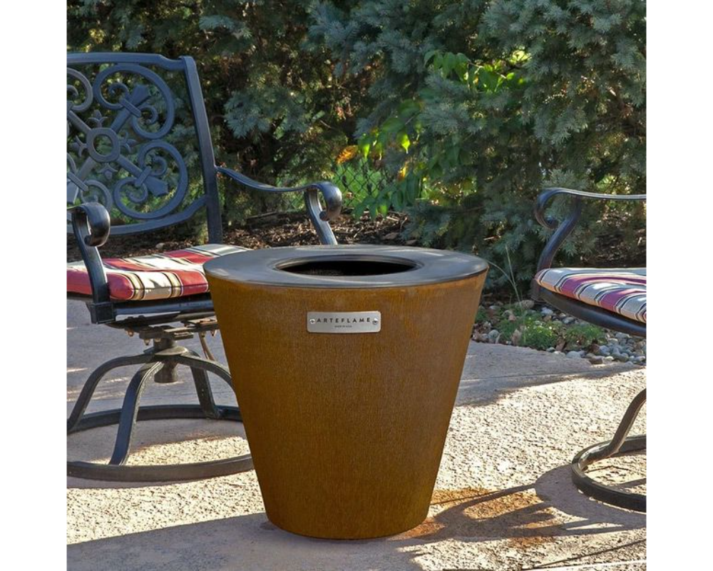 Arteflame One Series 20" Corten Steel Wood Fire Grill on outdoor patio surrounded by wrought iron garden chairs