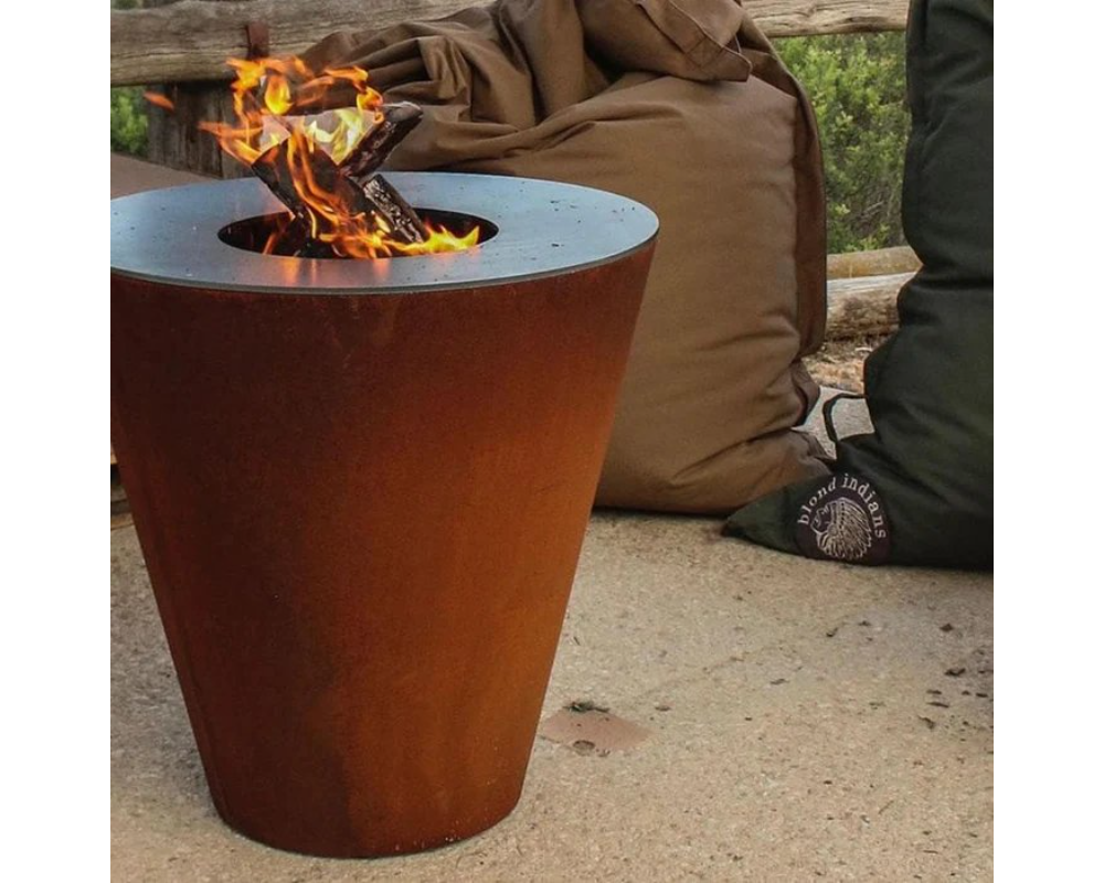 Arteflame One Series 20" Corten Steel Wood Fire Grill with open wood fire flame on outdoor patio with bean bag seating