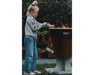 Arteflame One Series 20" Corten Steel Wood Fire Grill with child grilling vegetables on flat-top surface in backyard garden