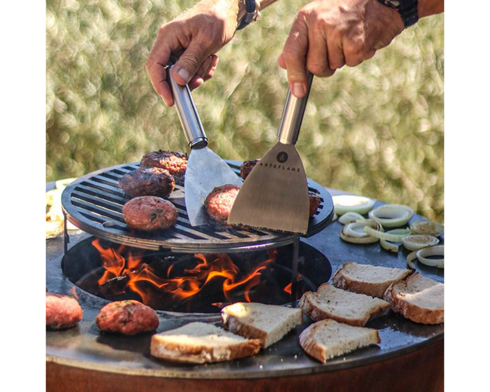 Arteflame One Series 30" Grill cooking burger patties and bread on flat-top steel surface with Arteflame spatulas over flame