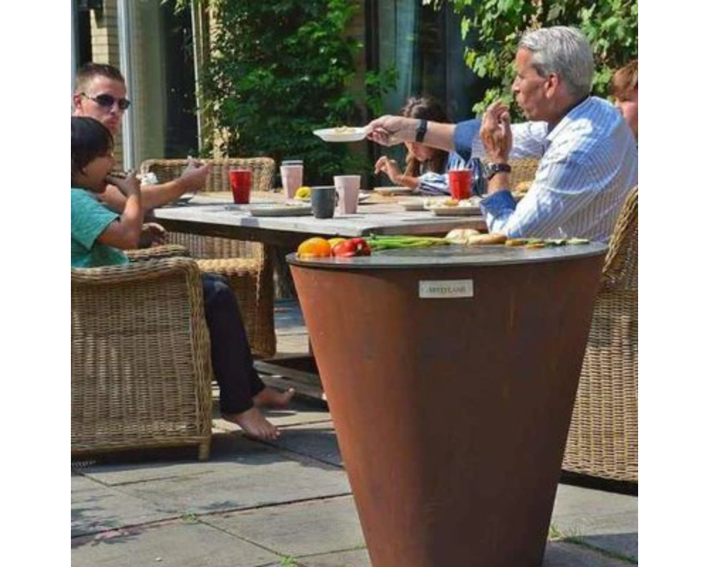 Arteflame One Series 30" Corten Steel Grill used as outdoor dining table with family eating on patio with wicker chairs