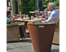 Arteflame One Series 30" Corten Steel Grill used as outdoor dining table with family eating on patio with wicker chairs