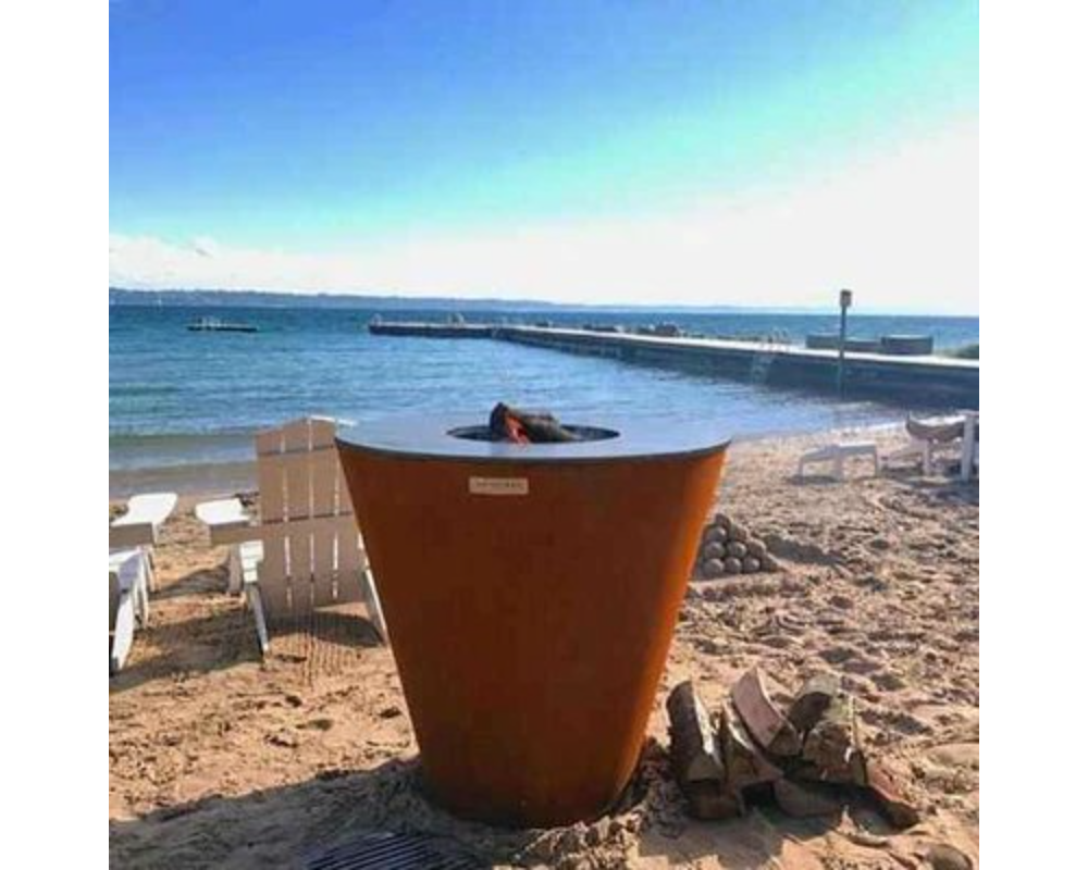 Arteflame One Series 30" Corten Steel Charcoal Grill on sandy beach with lakeside dock and Adirondack chairs