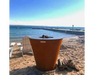 Arteflame One Series 30" Corten Steel Charcoal Grill on sandy beach with lakeside dock and Adirondack chairs