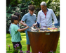 Arteflame One Series 40" Corten Steel Grill with family grilling burgers and vegetables together in backyard garden