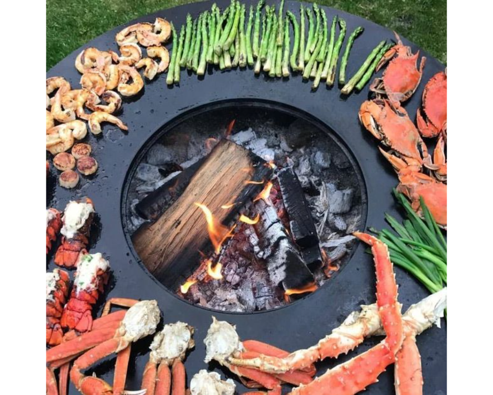 Arteflame One Series 40" Grill flat-top surface grilling shrimp, crab legs, lobster, and asparagus over open wood fire