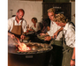 Arteflame One Series 40" Grill with chefs grilling food on flat-top steel surface at outdoor evening social gathering