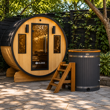 Wood barrel sauna with glass door beside a black cedar cold plunge ice bath in a garden