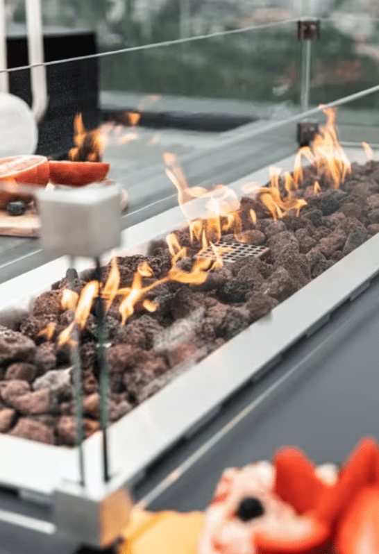 Elementi Granville fire pit table with flames and rocks, surrounded by a glass barrier
