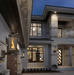 Travis Industries Tempest gas lanterns wall mounted flanking entrance of modern luxury home at night