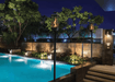 Pair of Travis Industries Tempest gas lanterns on in-ground posts flanking a luxury outdoor pool at night