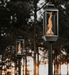 Pair of Travis Industries Tempest gas lanterns on in-ground posts with vortex flames burning at dusk in wooded outdoor setting