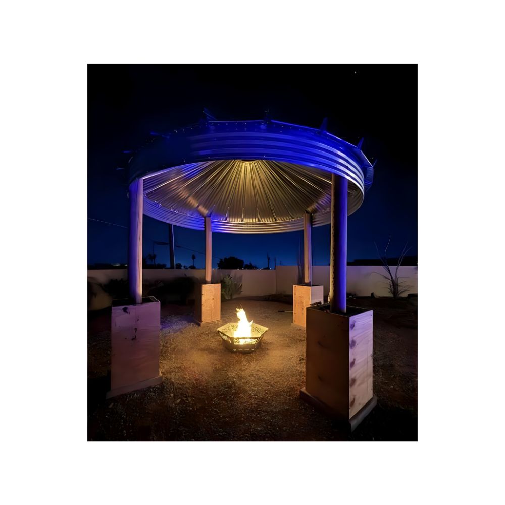 Grain bin gazebo with blue LED lighting and central fire pit at night — a dramatic outdoor feature for STR properties