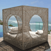 A large outdoor lounge cabana daybed with intricate geometric laser-cut metalwork, featuring two large circular openings, cream cushions, and a beachfront ocean view background.