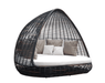 A dark woven wicker egg-shaped outdoor daybed with a white cushion and several beige and white throw pillows, shown against a plain white background.
