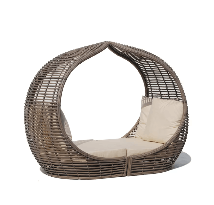 A modern teardrop-shaped wicker daybed with a curved back and seat, upholstered in a warm taupe-brown woven material and fitted with cream-colored cushions, shown on a plain white background.