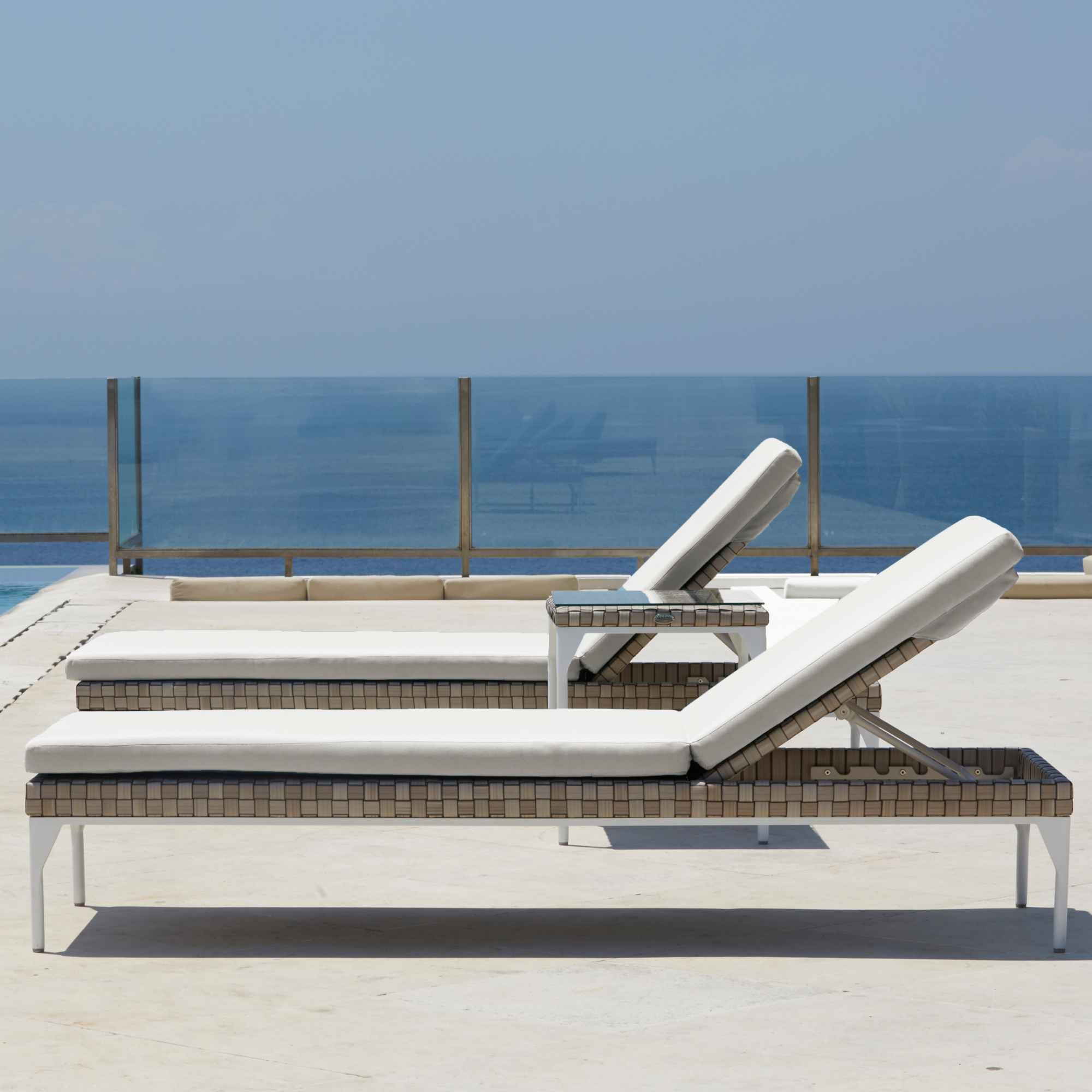 Two lounge chairs with white cushions on a balcony with a clear blue sky and ocean view.