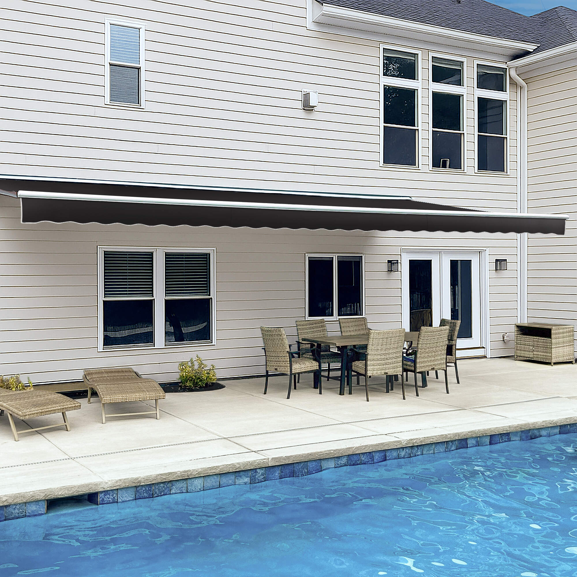 Awntech Destin motorized retractable awning in black extended along a cream siding house over a poolside dining set