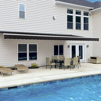Awntech Destin motorized retractable awning in black extended along a cream siding house over a poolside dining set
