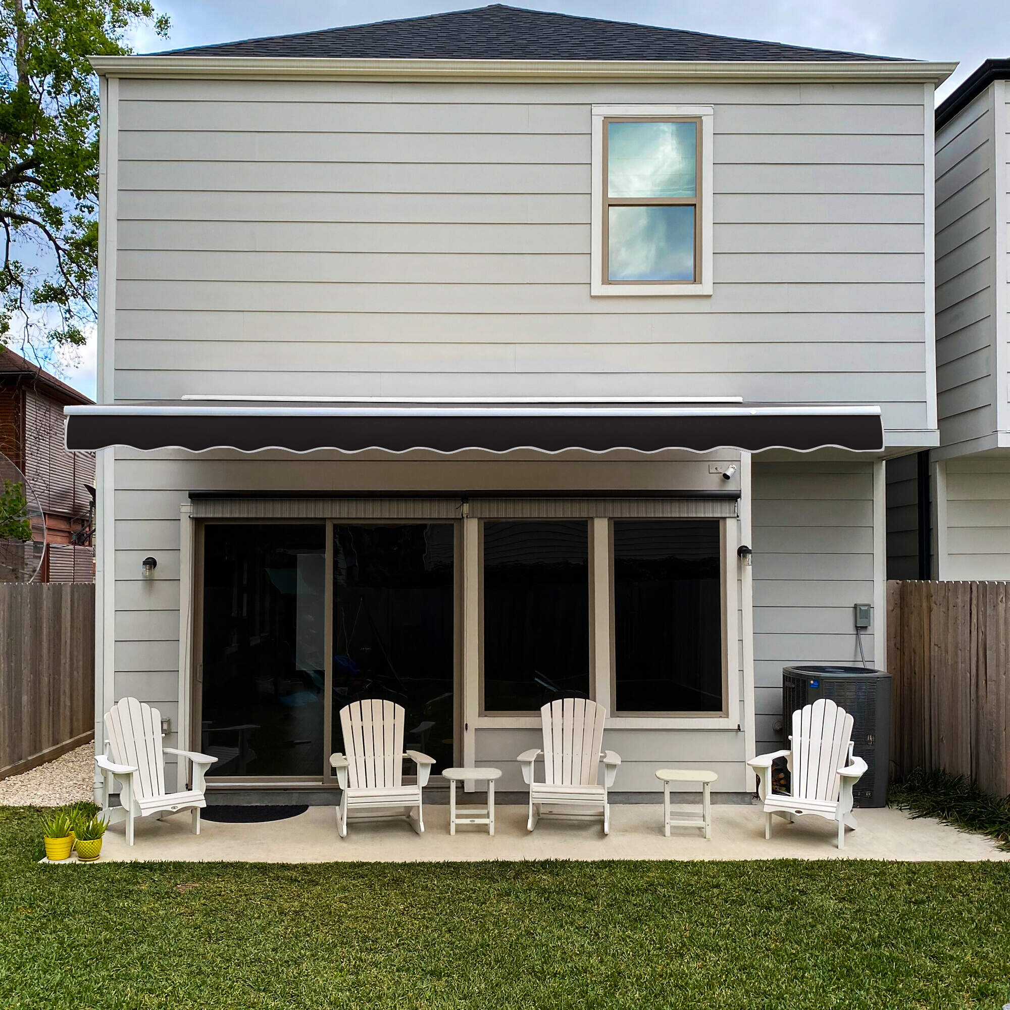 Black Awntech Destin motorized retractable awning with white hood extended over a patio with four white Adirondack chairs