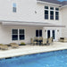 Awntech Destin motorized retractable awning in gray extended along a cream siding house over a poolside dining set