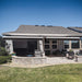 Two black Awntech Key West full cassette retractable awnings mounted under the eave of a one story house over a paver patio with a stone seat wall