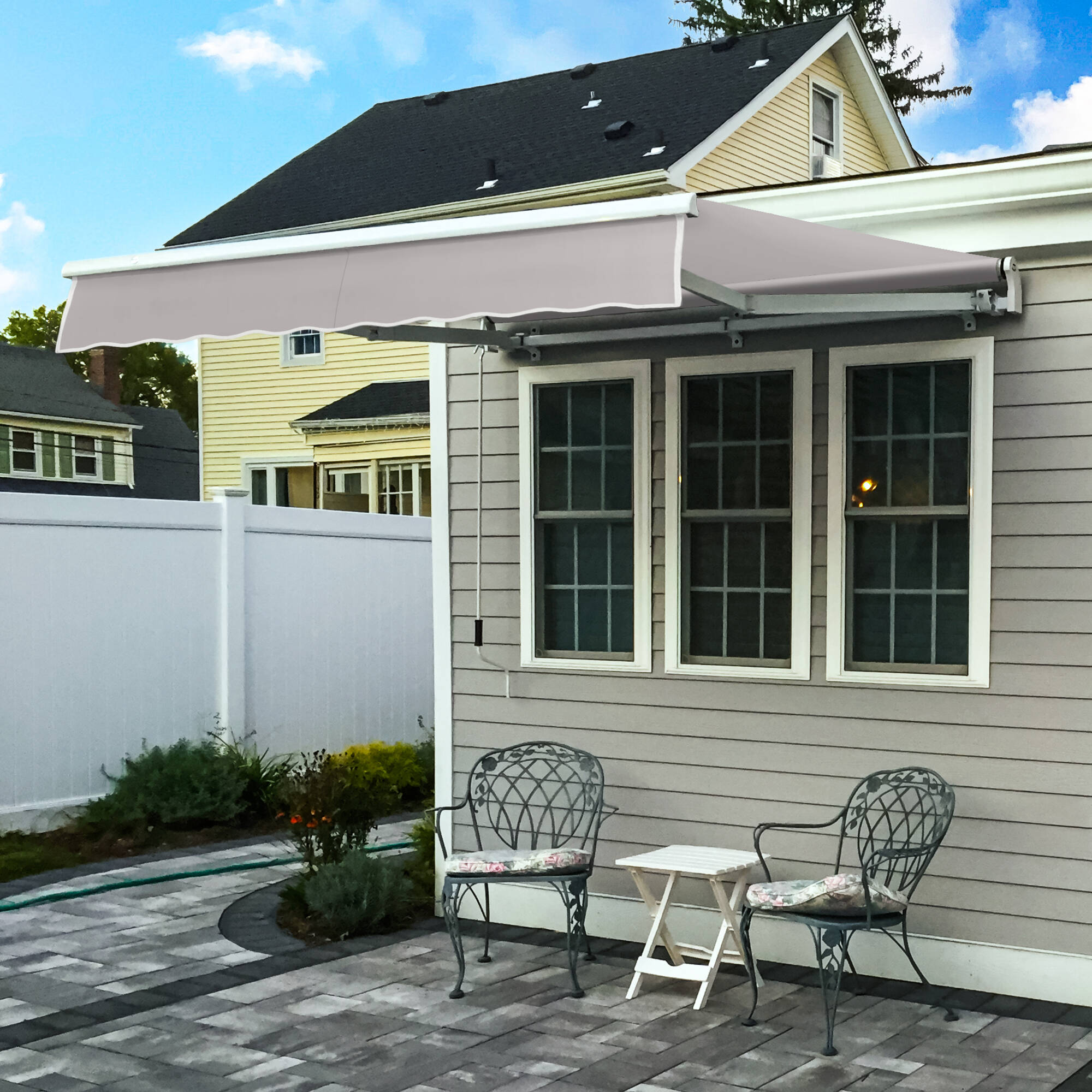 Awntech Maui motorized retractable awning in light gray acrylic extended over a paver patio beside a gray clapboard house