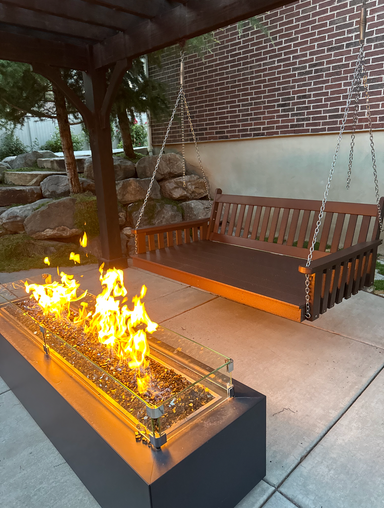 Customer photo: A&L Poly Traditional swing bed in Tudor Brown hung from a backyard pergola, with a lit fire pit in the foreground