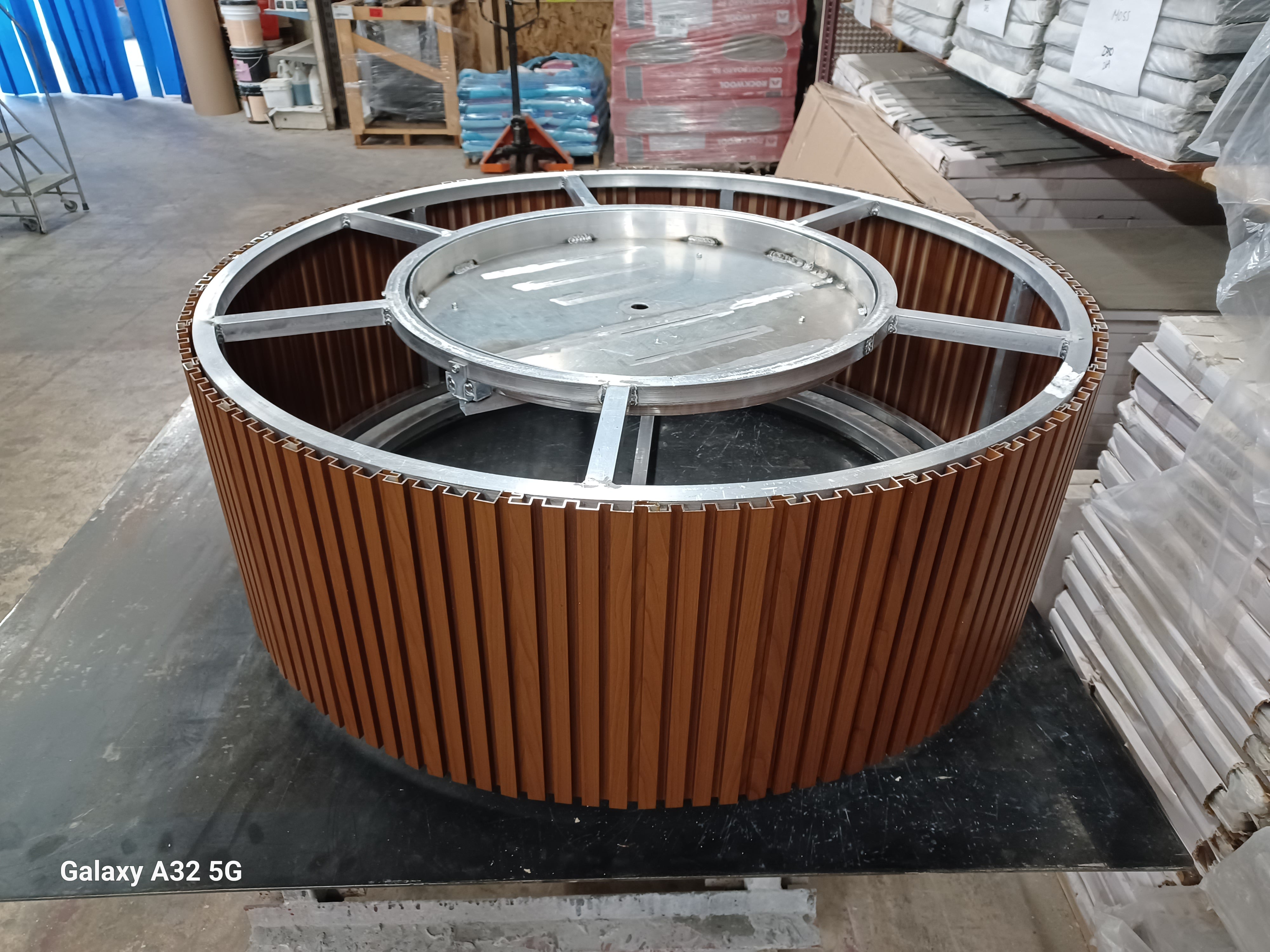 Firefly 48-inch round fire pit frame with vertical wood-look aluminum cladding and burner tray, in production