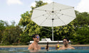 Guests relaxing in a pool under a Ledge Lounger Ultra cantilever umbrella