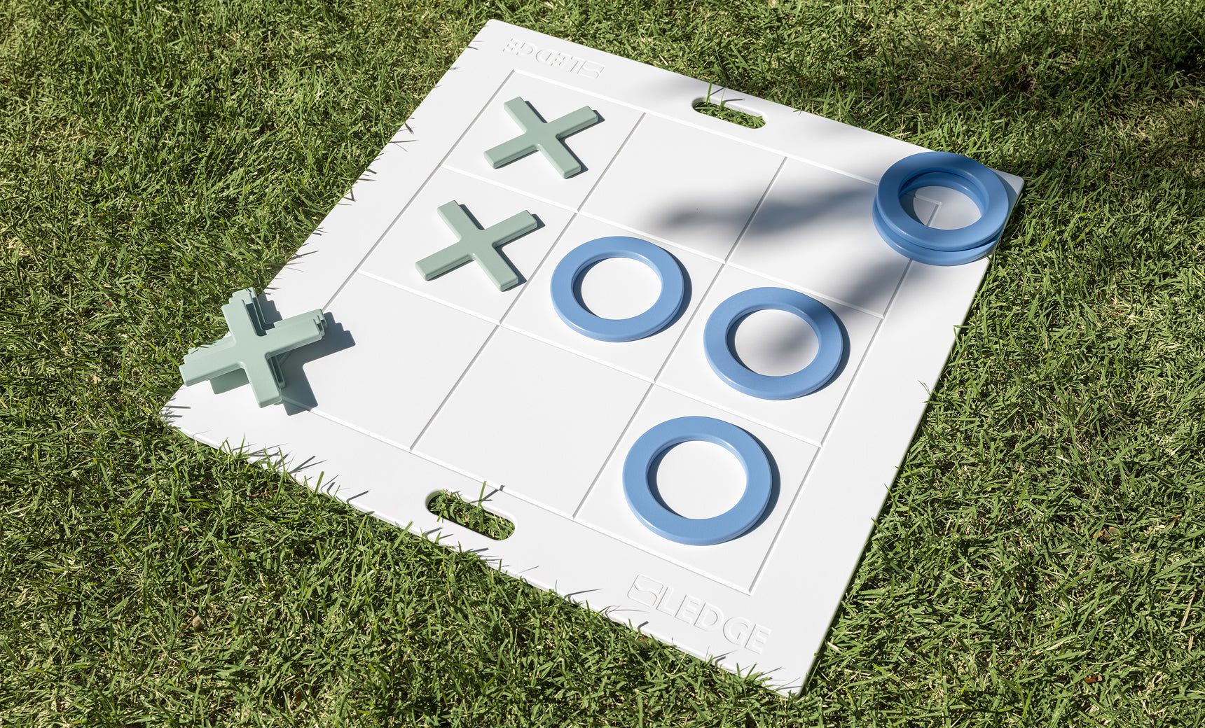 Giant white tic tac toe board with blue Os and green Xs on the grass, three Os lined up across the middle row