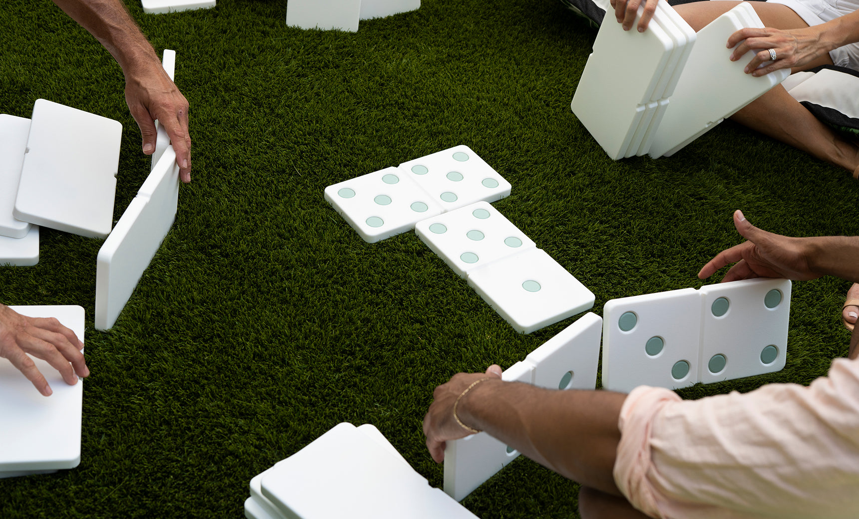 Group of people laying out large white dominoes on a green lawn